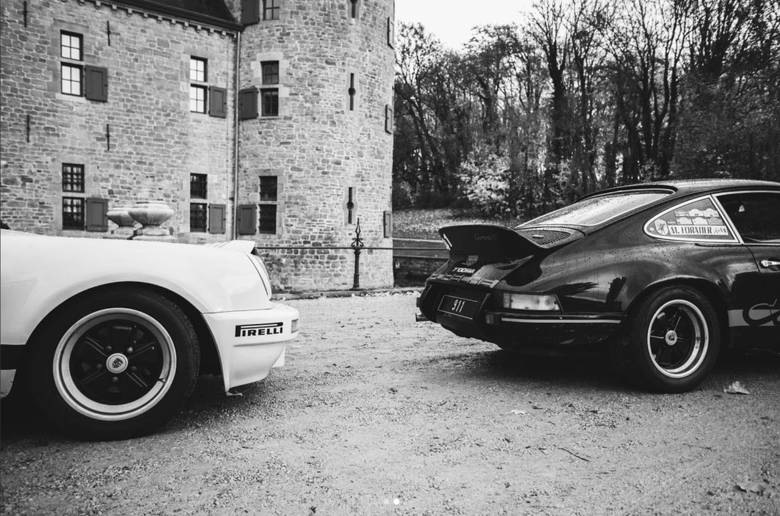 Two classic Porsche sports cars parked facing each other in a gravel courtyard beside a stone castle, black-and-white photo. Two classic Porsche sports cars parked facing each other in a gravel courtyard beside a stone castle, black-and-white photo.
