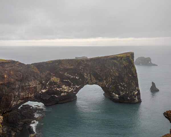 Wall decor photo of Dyrhólaey natural arch in Iceland showing black cliff and ocean under dramatic sky, perfect for Nordic interior decoration