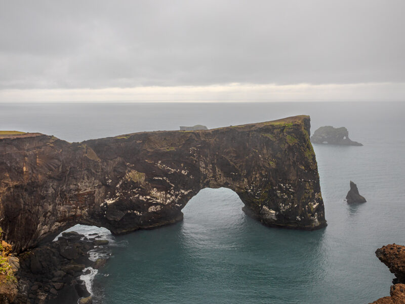 Wall decor photo of Dyrhólaey natural arch in Iceland showing black cliff and ocean under dramatic sky, perfect for Nordic interior decoration