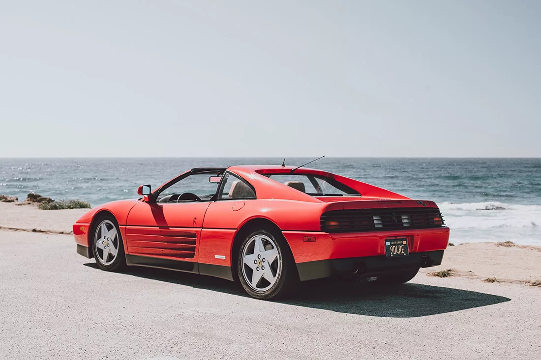 Red Ferrari 348 TS parked facing the ocean on 17-Mile Drive at Pebble Beach, California, rear three-quarter view