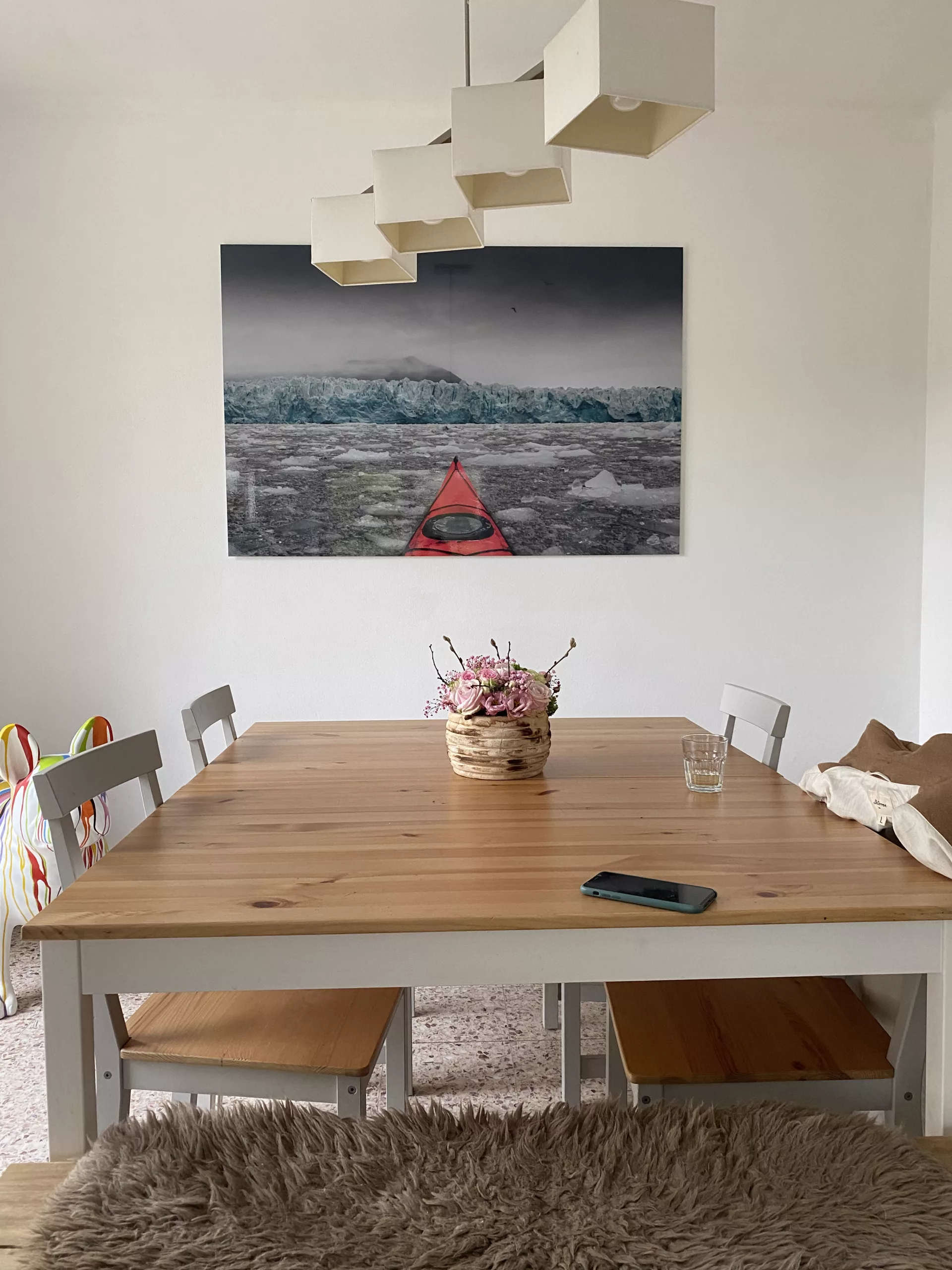 Fine art print installed above a wooden dining table with black chairs — Cars and Roses