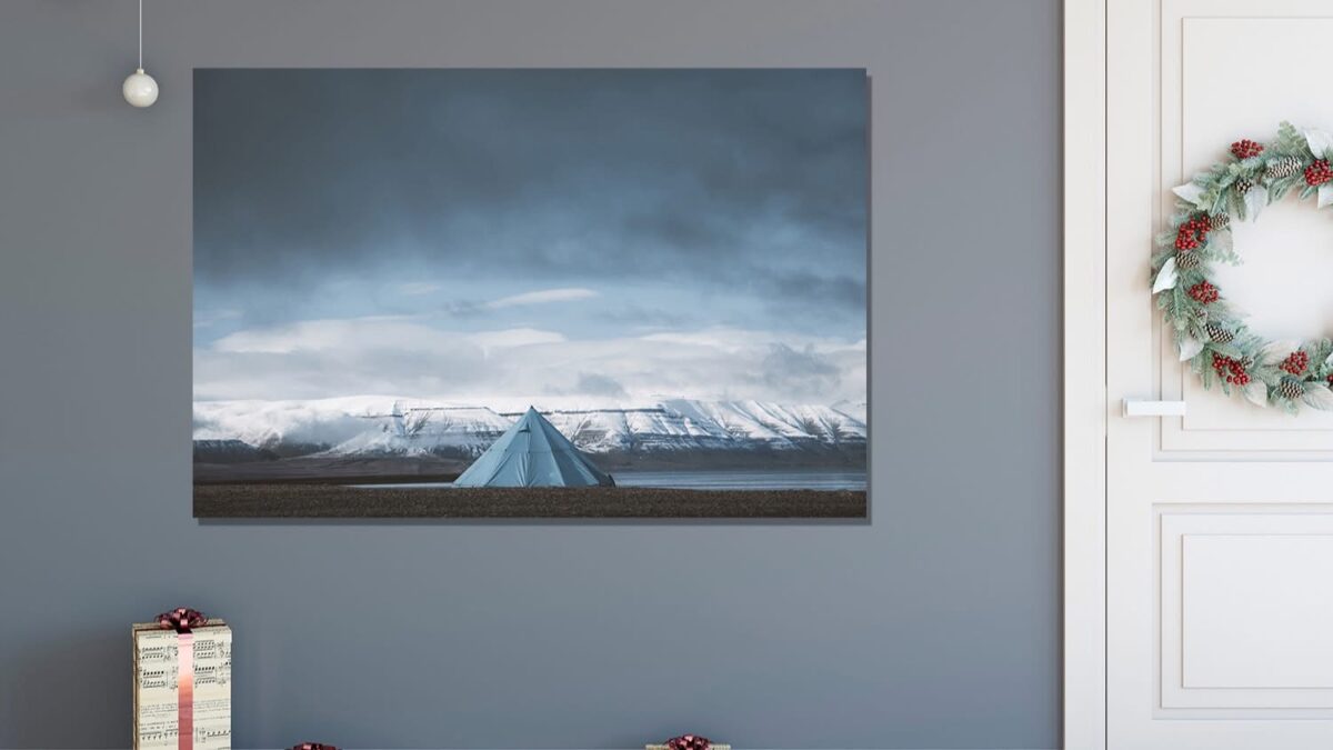Snowy mountain landscape photography under a dramatic sky with a tent in the foreground, presented in a festive interior with Christmas decorations - Cars and Roses wall art