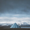 Photo Svalbard tente Fjord Svalbard photography showing a solitary blue tipi tent facing snow-capped mountains of the arctic fjords under a dramatic sky