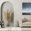 empty poster frame on beige wall in living room interior with mo Svalbard photography showing a solitary blue tipi tent facing snow-capped mountains of the arctic fjords under a dramatic sky