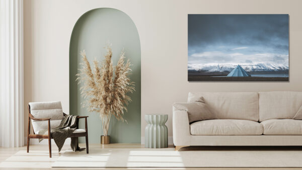 empty poster frame on beige wall in living room interior with mo Svalbard photography showing a solitary blue tipi tent facing snow-capped mountains of the arctic fjords under a dramatic sky