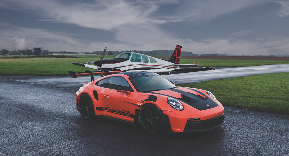 Dynamic photograph of an orange Porsche 911 GT3 RS showcasing its aggressive aerodynamics, distinctive rear wing, and race-inspired design against a dramatic backdrop
