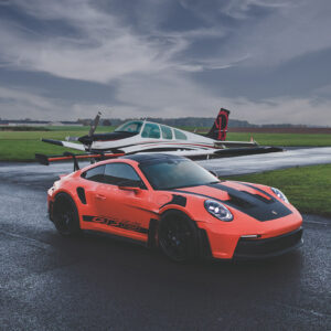 Dynamic photograph of an orange Porsche 911 GT3 RS showcasing its aggressive aerodynamics, distinctive rear wing, and race-inspired design against a dramatic backdrop