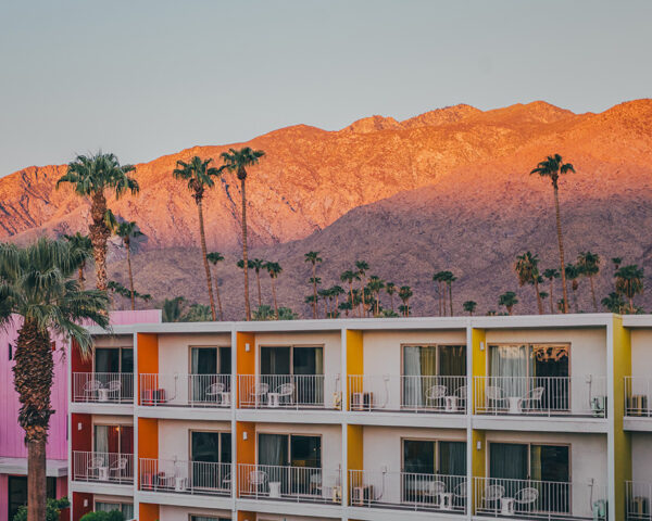 The Saguaro Hotel with colorful pink orange yellow facades at sunset with San Jacinto Mountains and palm trees in Palm Springs California
