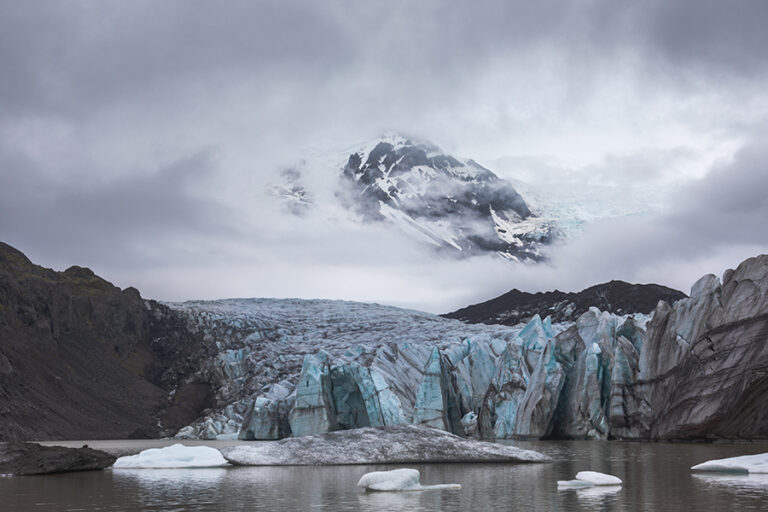 Dramatic landscape photograph of Svinafellsjökull Glacier in Vatnajökull National Park, Iceland, showcasing blue ice formations against dark mountains under a moody sky