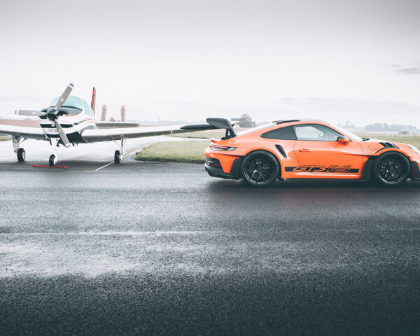 Orange Porsche 911 GT3 RS on a wet airfield runway beside a light aircraft - fine art photography print