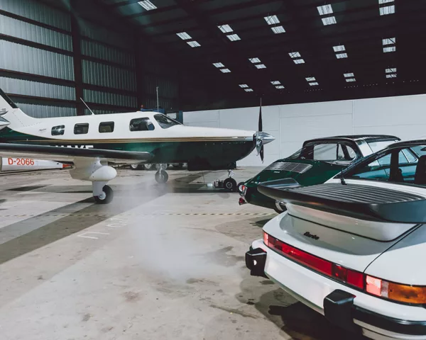 White Porsche 911 Turbo and green 911 in front of a Piper Malibu in a hangar lit by skylights - fine art photography print