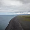 Iceland black sand beach photograph Black sand beach on the coast of Iceland seen from above, with the grey Atlantic, green plains and snow-capped mountains