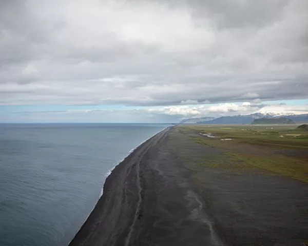 Iceland black sand beach photograph Black sand beach on the coast of Iceland seen from above, with the grey Atlantic, green plains and snow-capped mountains