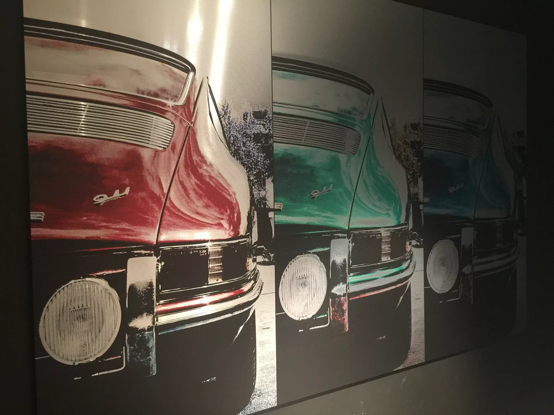 Close-up of a brushed aluminium print showing the rear of a Porsche 911 in red, green and blue panels
