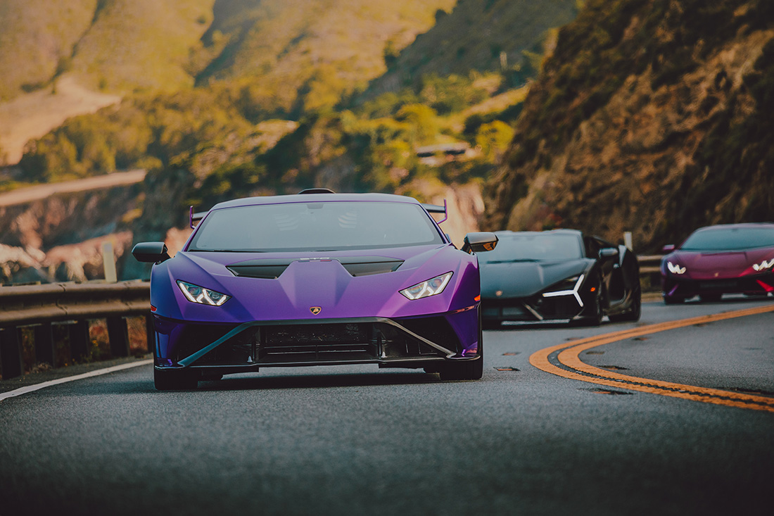 Purple Lamborghini Huracán at the front on a winding mountain road, followed by two other sports cars.