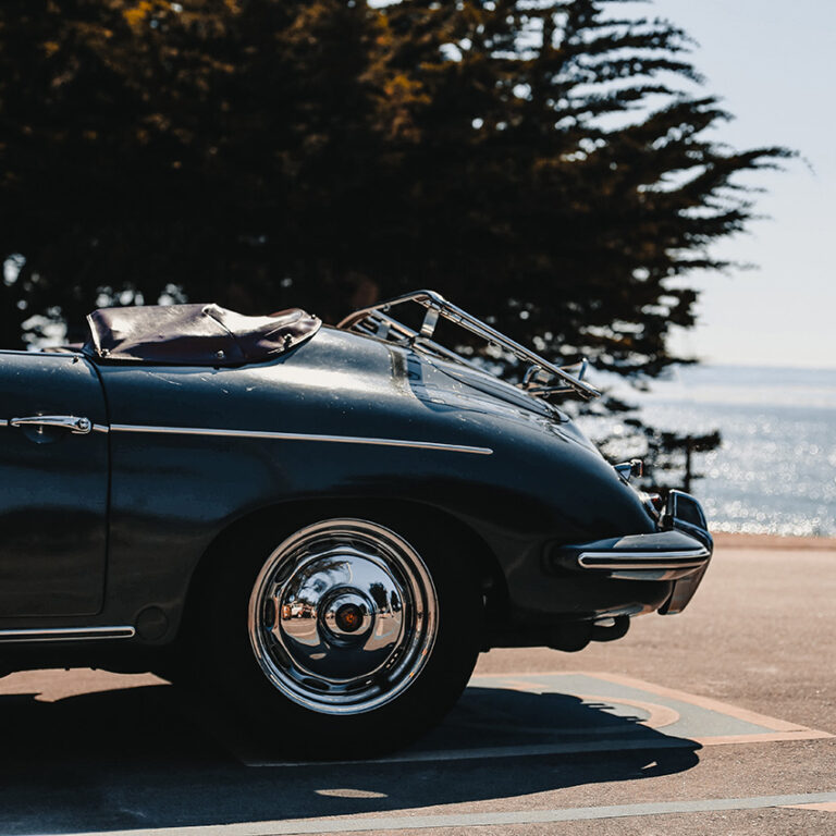 Classic vintage car parked near the water, reflecting sunlight on its shiny chrome wheel. material to print photos on