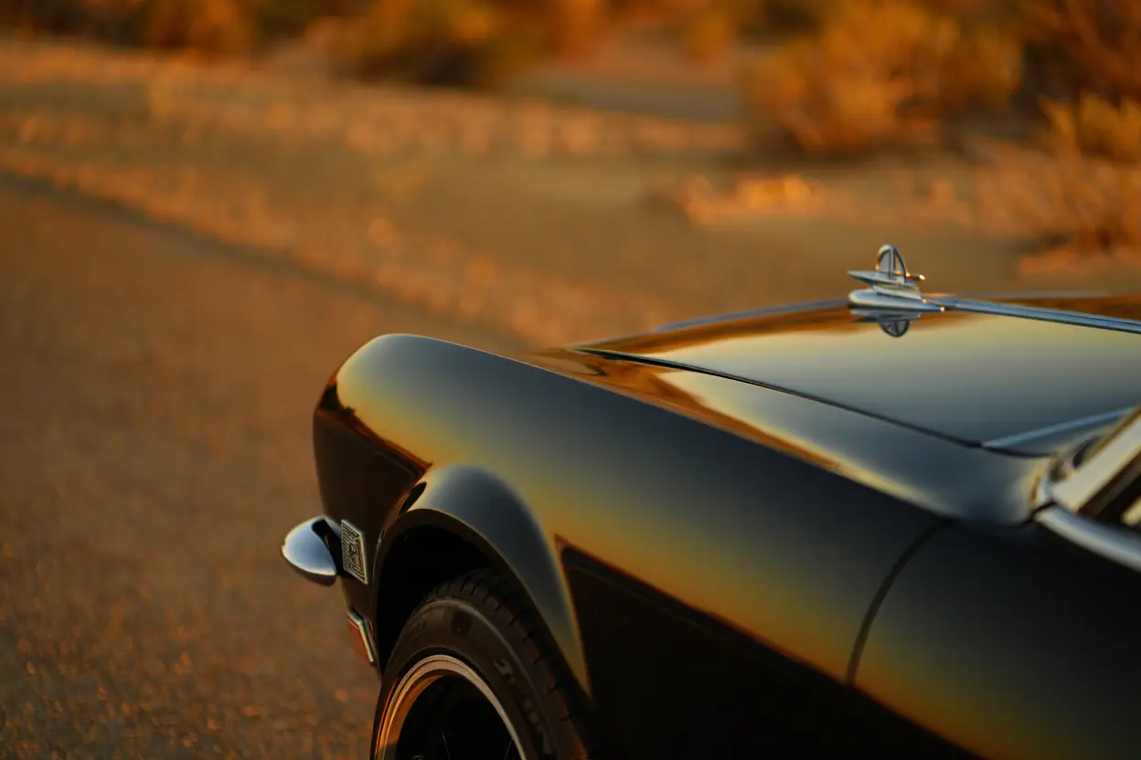 Close-up of a sleek black car at sunset, highlighting its curved fender, chrome details, and glossy hood with warm orange reflections. rule of thirds in car photography