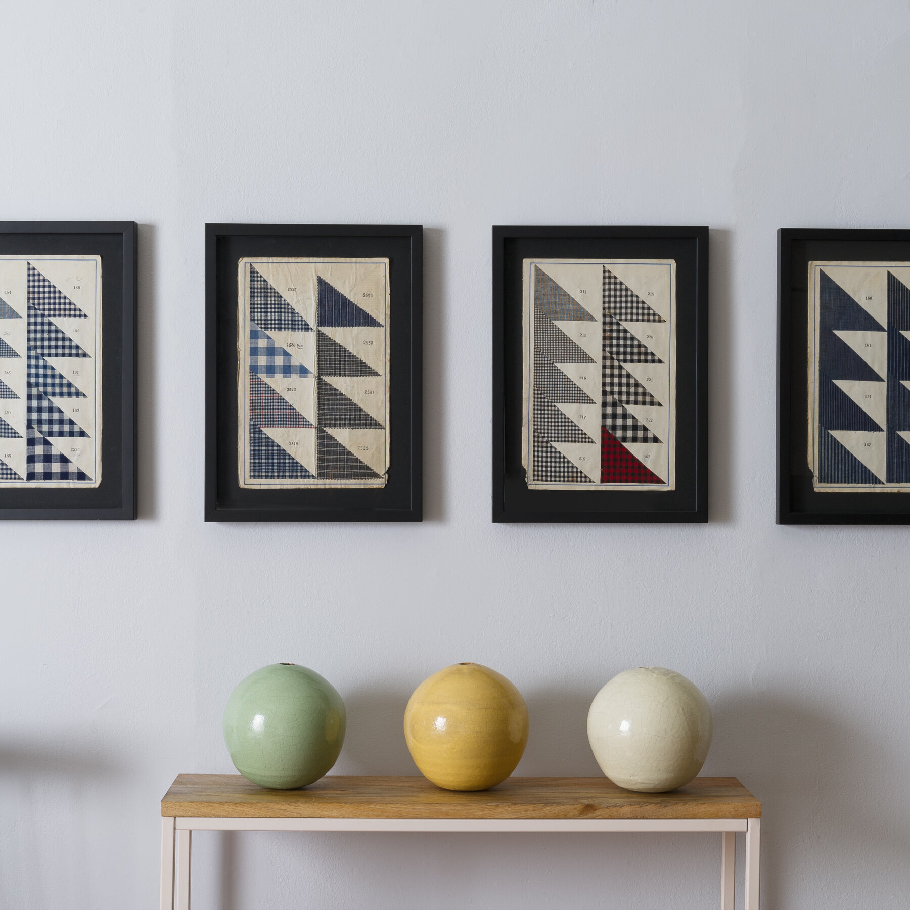Four framed geometric prints hang in a row above a small wooden console, with three colorful ceramic spheres displayed on the surface. How to hang wall art is illustrated by the evenly spaced frames and neat arrangement.