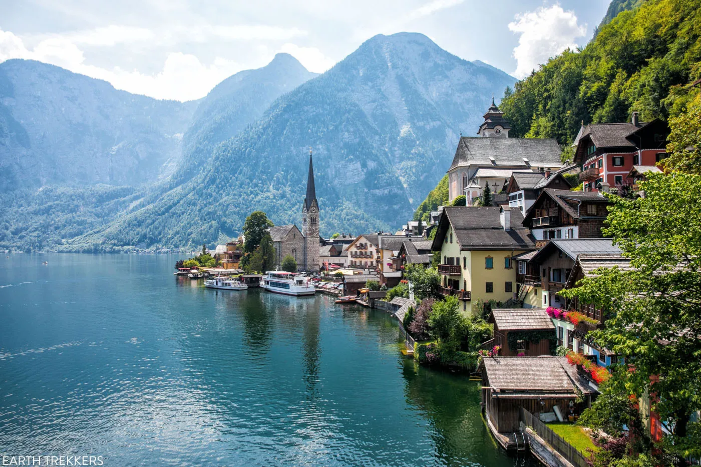 Lar idyll on the water: a village hugs the lakeshore with colorful houses, a church steeple, and boats, set against towering mountains. photography destinations in europe integrated.