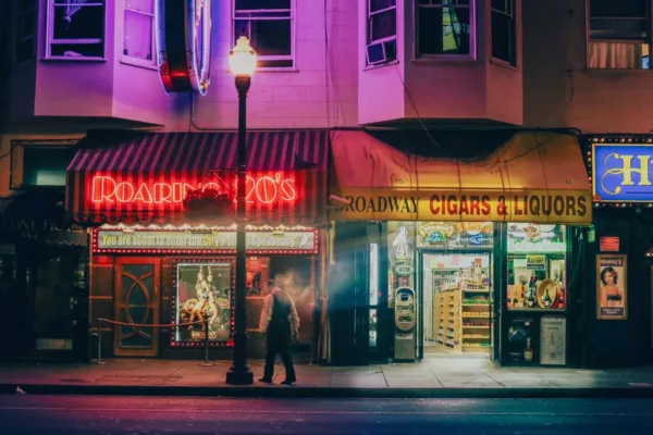 san-francisco-nuit-broadway-v2-900x600-1.webp Fine art photograph of Broadway in San Francisco at night: red Roaring 20’s neon sign, lit street lamp and a passer-by in motion