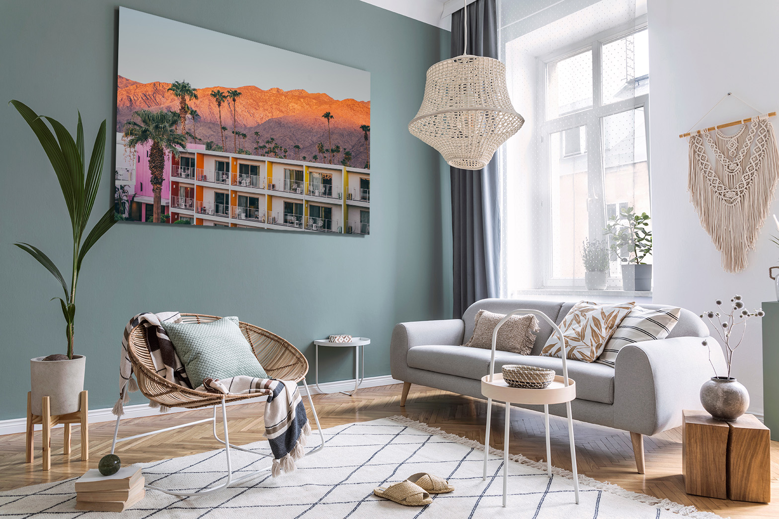 A stylish living room with a teal accent wall, a large framed sunset photograph, a gray sofa, woven chair, and hanging wicker light fixture. Includes plants, a rug, and natural wood accents. How to hang wall art fits naturally in a serene home setup.
