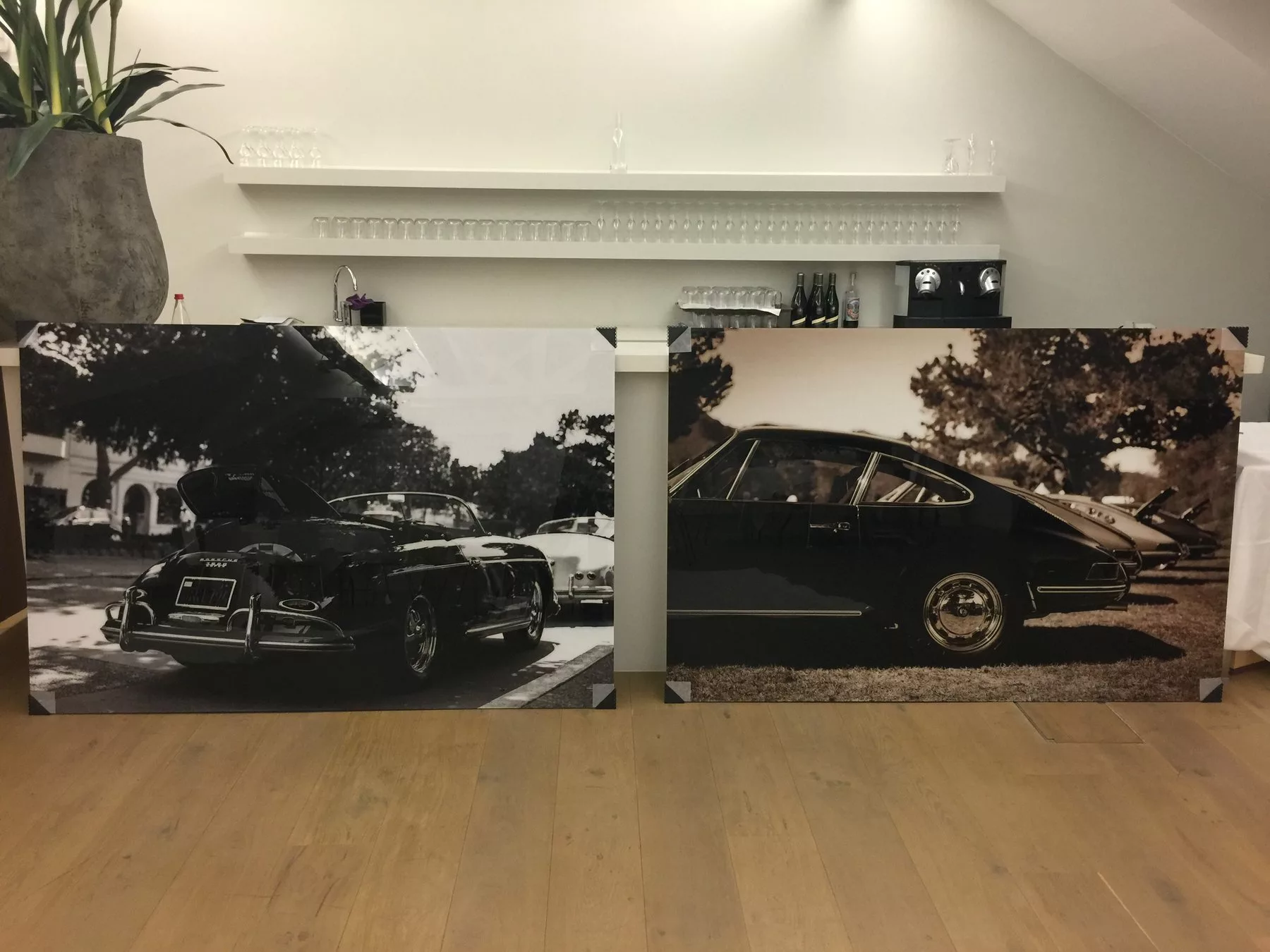 Two 180×120 cm acrylic glass prints, a black and white Porsche 356 and a sepia row of Porsche 911s, unboxed and leaning against a counter