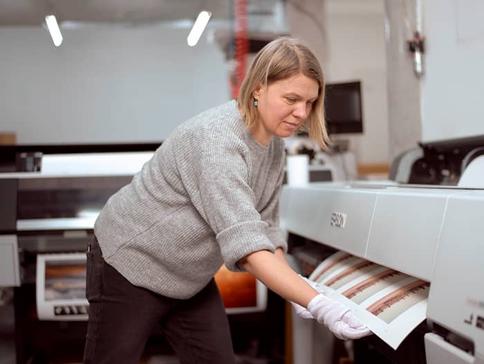 A woman using a large printer in a print lab, loading paper for high quality photo printing online.